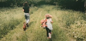 Foto aus dem Buch-Cover Johanna Constantini "Angehörige Leben Länger - Mutmacher für die Demenzbegleitung" - erwachsene Person, ein Kind mit Stofftier und ein kleiner Hund laufen auf einem Weg im Wald
